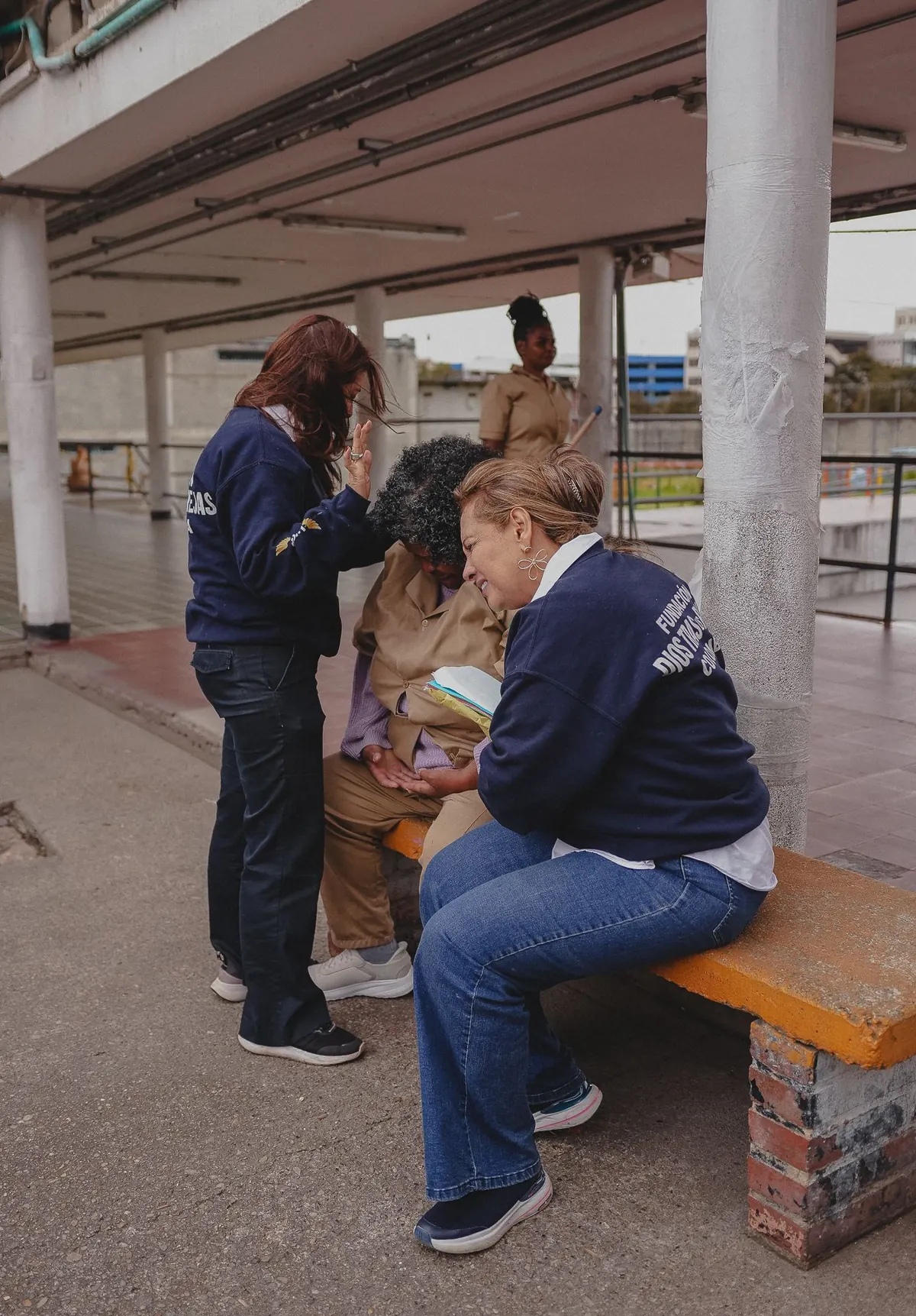Dos mujeres de la fundación oran junto a una mujer en una banca del patio.